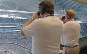 Two ATC spotters observe play on the field through binoculars.